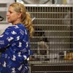 A blonde-haired woman is holding a puppy in front of dogs being held in crates