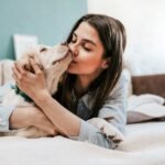 A woman is kissing a dog in bed