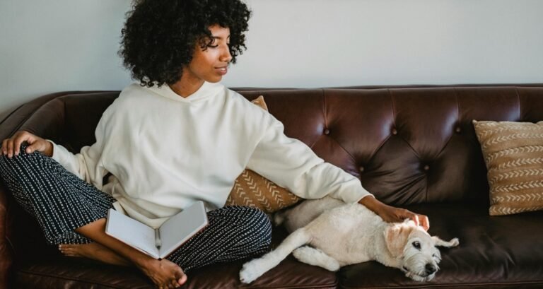 A woman is studying on the couch with her dog