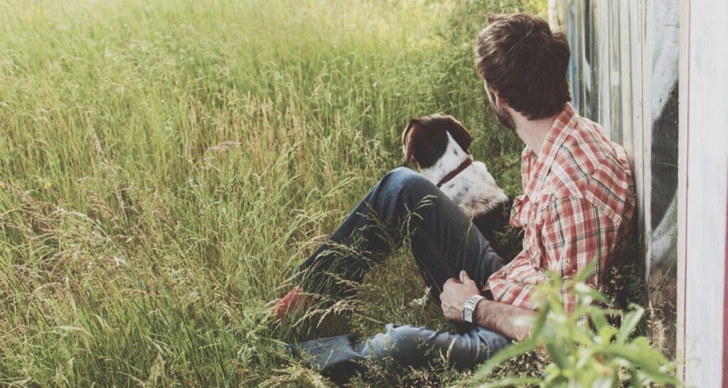 A man is sitting with a dog in the grass outside