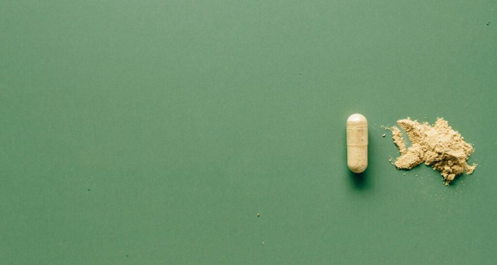 An open and closed supplement capsule in front of a green background