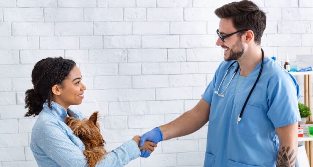 A male veterinarian is shaking a female dog owner's hand