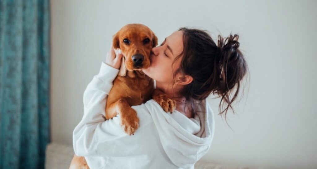 A woman is kissing a dog in their arms